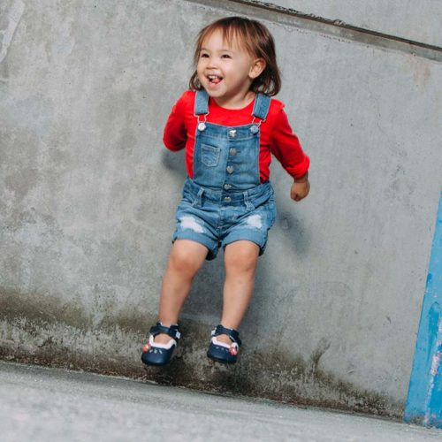 A toddler jumping while wearing a blue pair of Charlotte children's barefoot shoes by Jack & Lily